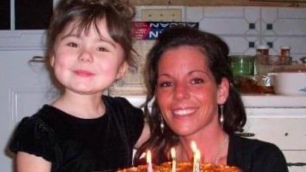 A mother and young girl pose with a lit birthday cake.