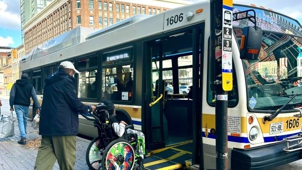 man pushes person using a wheelchair onto a city bus