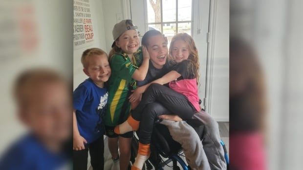 A boy in a wheelchair is surrounded by his younger siblings, one of whom is sitting in his lap. 