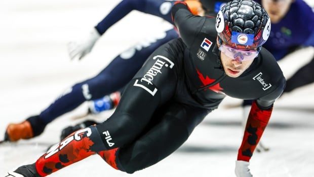 A male short track speed skater touches the ice with his left glove as he rounds a corner.