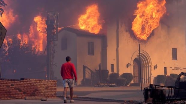 A man in red sweatshirt walks in front of a burning church