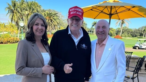 A woman, and two men pose for a picture next to a sunny golf course.