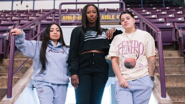 Three women stand alongside each other on a basketball court.