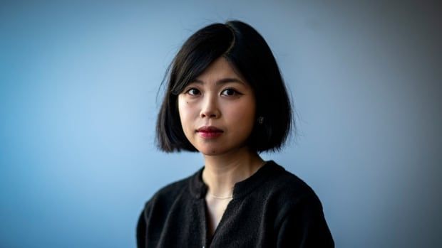 An East Asian woman in her 20s poses in front of a blue background.