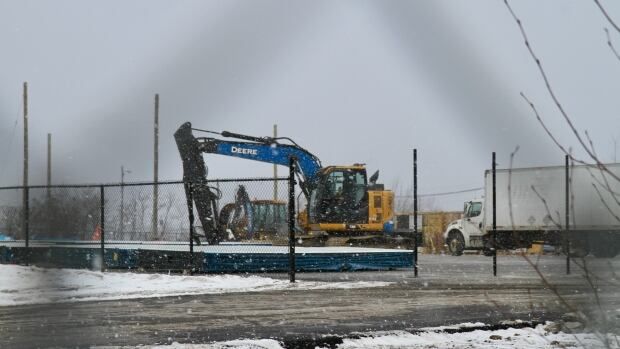 A construction vehicle is parked beside slabs on asphalt as it snows