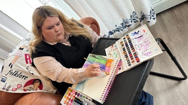 A woman sits in her living room using watercolours to paint.