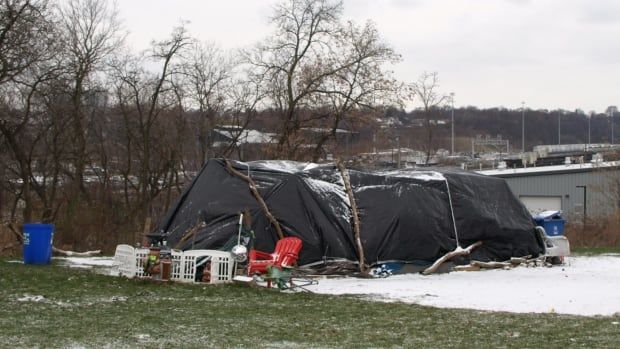 A tent covered in a black tarp surrounded by a plastic chair and a fence.