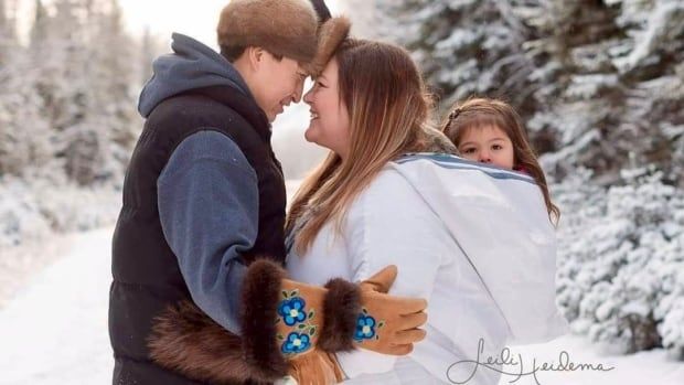 A man and a woman in traditional winter outfits. They're holding each others arms, facing each other, and the woman has a baby on her back.