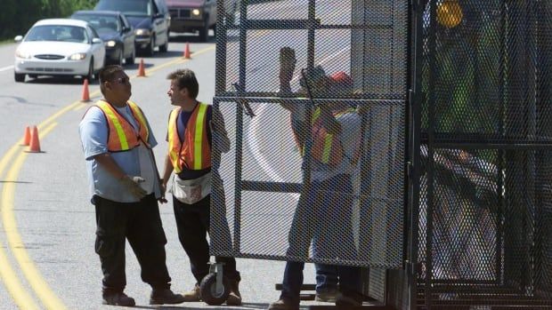 Three men set up a gate on a highway with traffic forming behind them.