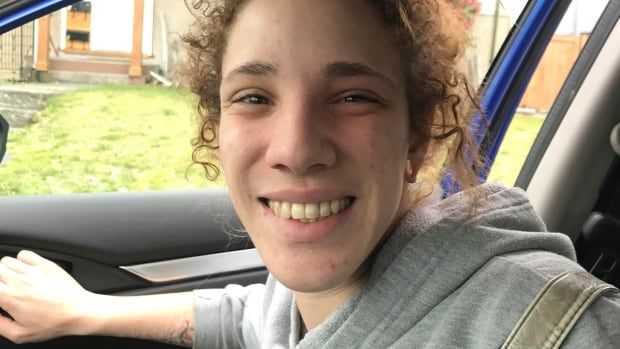 A teenage girl wearing a grey hoodie smiles while exiting a car.