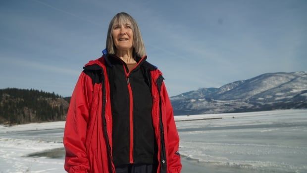 A woman with grey hair in a red snow coat stands by an icy reservoir near Edgewood B.C.