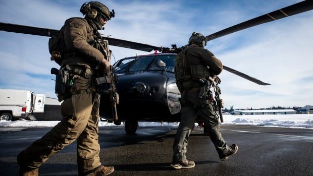 Two heavily-armed soldiers are seen walking towards a helicopter on a snowy day.