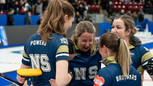 A women's curling team smiles while wrapping their arms around each other in celebration.