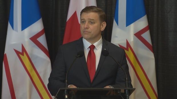 A man at a podium in a suit and red tie.