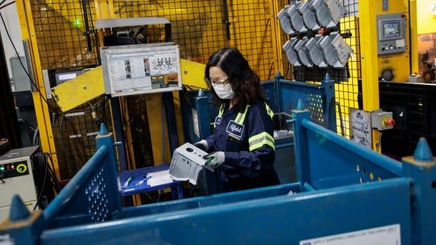 A worker in navy coveralls with hi-vis striping and safety goggles uses a machine to stamp out vehicle components.