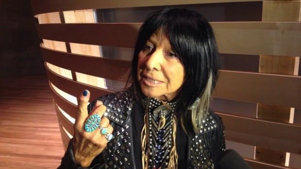 A woman in a leather jacket speaks to reporters in a darkened room.