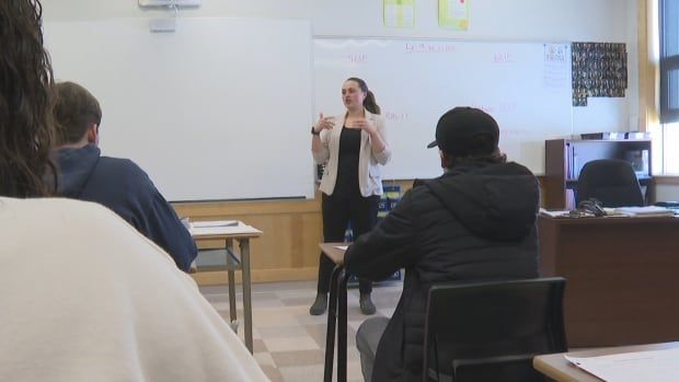 Female teacher stands at the front of the classroom of students.