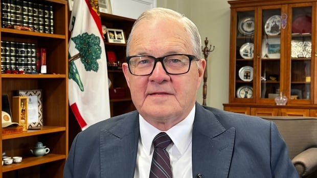 A man in a suit and glasses smiles at the camera in an office