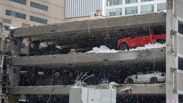 Two vehicles near a collapsed section of a parking garage on a snowy day.