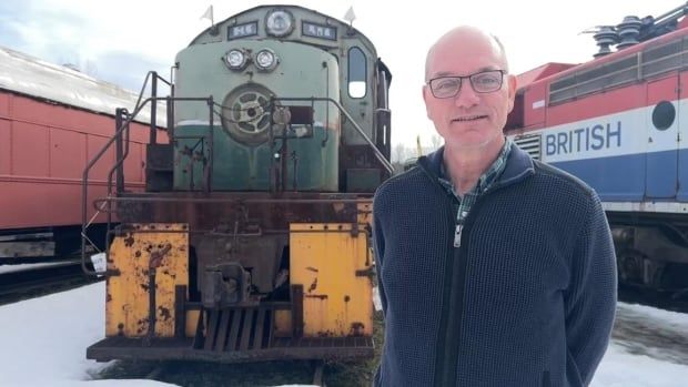 Man stands in front of a train in winter.