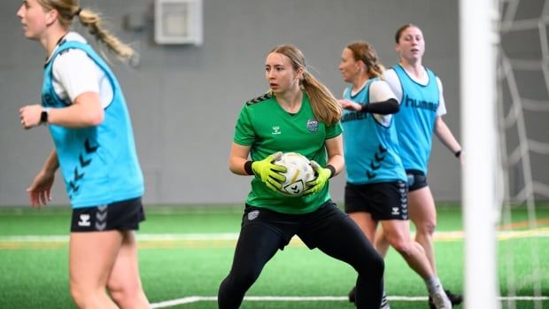 A soccer goalkeeper holds the ball, as opposing players surround her.