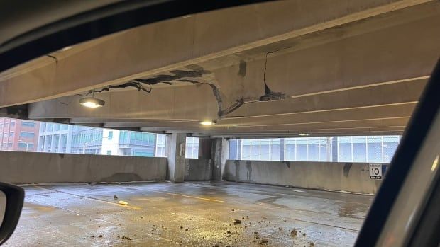 A photo of the inside of a parking garage, where the concrete of the roof is crumbling.