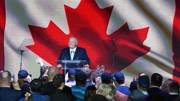 A man in a blue suit is seen on stage in front of a Canadian flag.