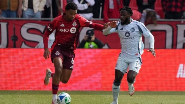 A male soccer player controls the ball as he evades an opponent during a day game.