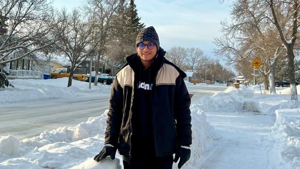 A man in a tuque and winter jacket stands on a snowy street.