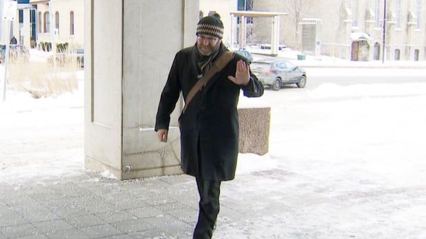 A man walking in winter, holding up his hand.