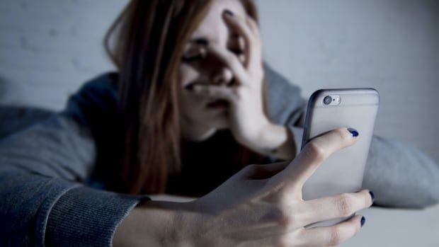 A young woman holding a cellphone closes her eyes and puts her other hand over her face.