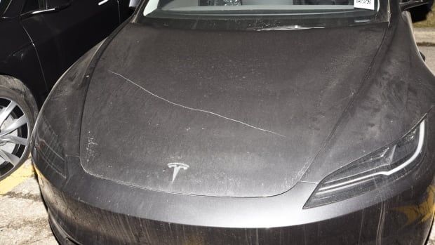 A dark Tesla car with a scratch over it's hood. 