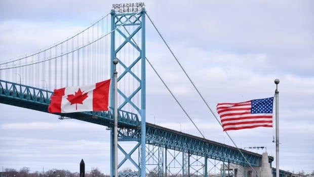 A Canadian and U.S. flag in front of a bridge.