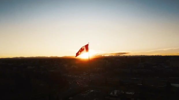 A Canadian flag flies on a pole in front of a sunset.