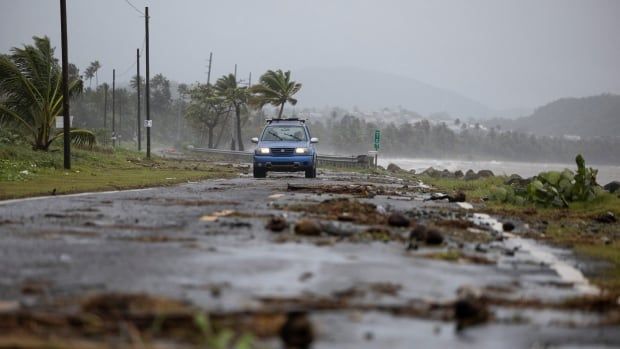 A car drives through a seaside road littered with debris