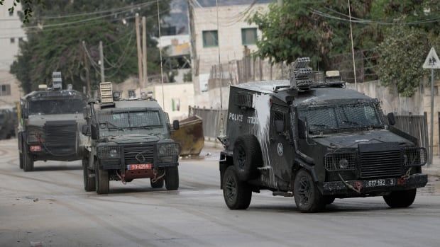 Three armoured vehicles drive down a street. 