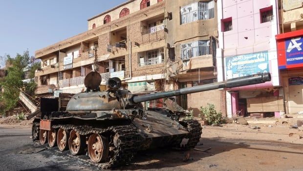 A damaged tanks is parked on a road in front of a line of buildings. 