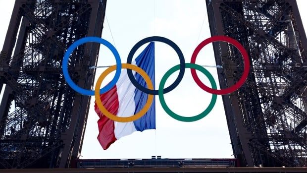 The Olympic rings -- five interlocking circles in blue, yellow, black, green and red -- hang from the façade of the Eiffel Tower, the French flag fluttering behind them. 