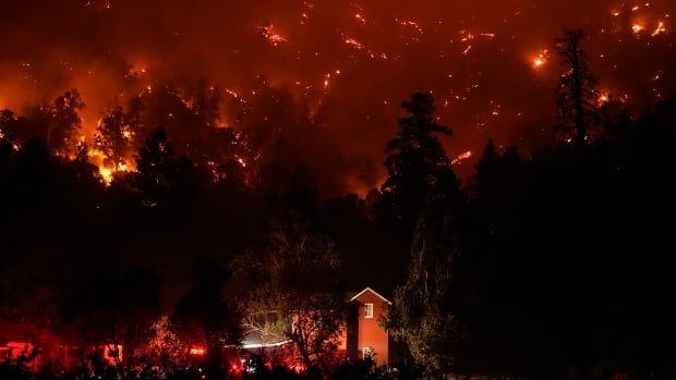 A house in the foreground as fire consumes hillsides in the background