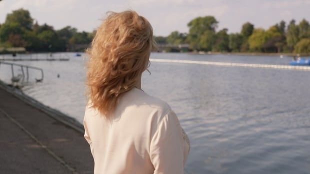 A woman with her back to the camera looks out across a river.