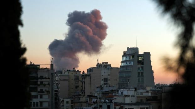 Dark grey smoke rises from buildings in a city suburb at dusk.