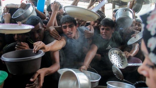 Young boys holding pots and bowls reach their arms for food.