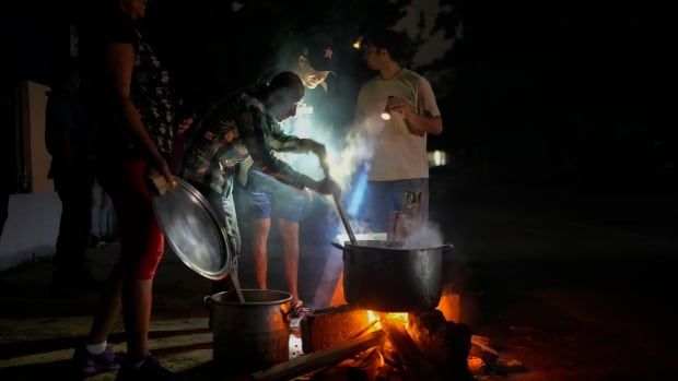 People cook soup over an open fire, at night on a street.