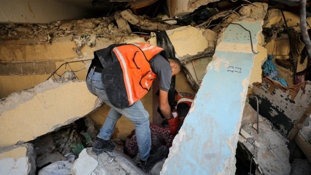 A man in an orange vest looks through rubble 