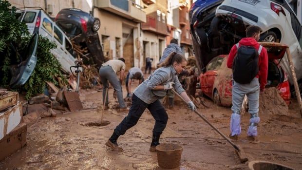 People use brooms to clear mud on a road strewn with debris and piles of upturned cars.