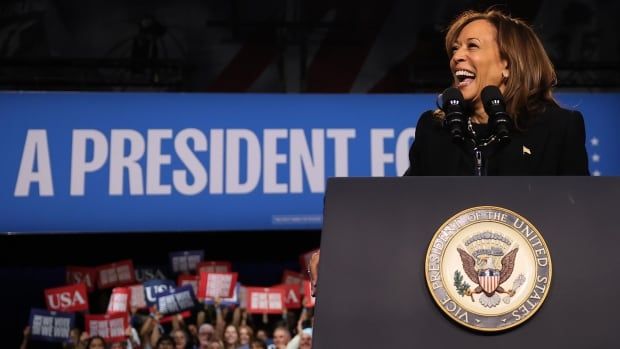 A woman in black laughing at a podium. A crowd is behind her.