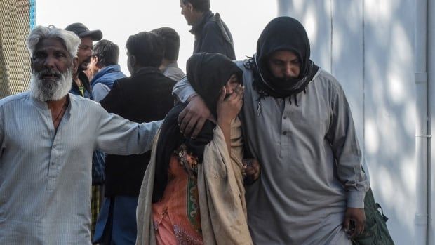 A woman is comforted by two men as they walk.