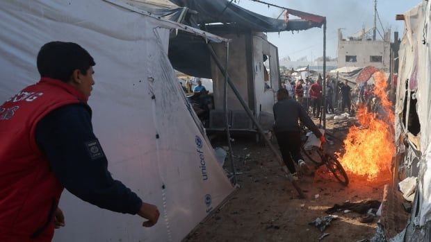 A person with a bike runs away from a fire burning in between tents at a refugee camp.