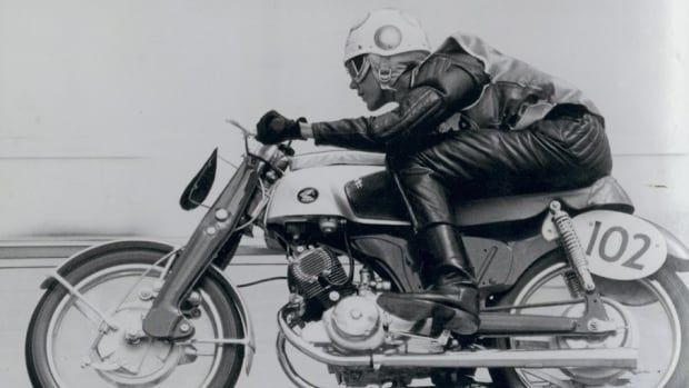 Black and white photo of a leather-clad woman riding a motorcycle