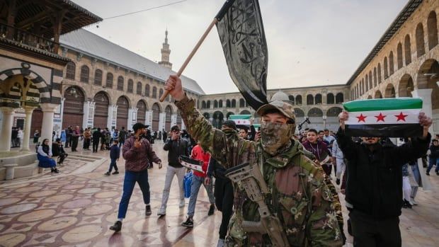 A masked man in militia  gear waves a flag in a town square